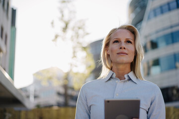 Thoughtful female professional looking away while holding digital tablet at financial district