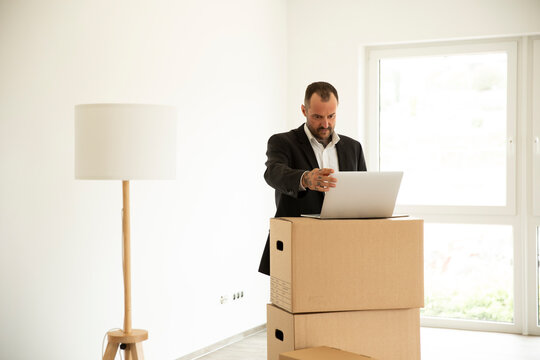 Businessman working over laptop on stacked boxes in new house