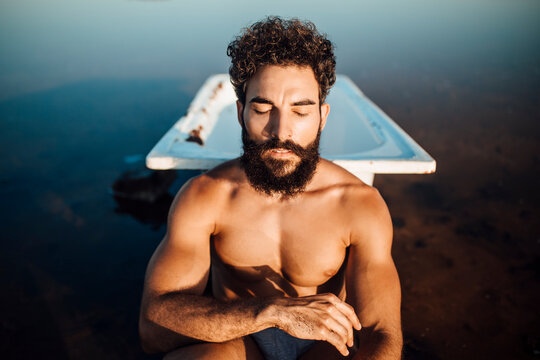 Bearded man sitting against bathtub in lake
