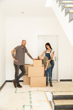 Family with cardboard boxes standing against wall in new apartment