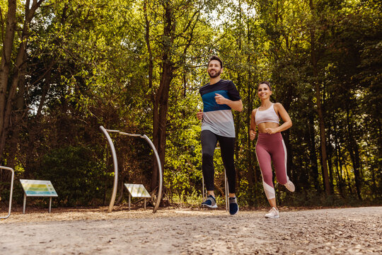 Sporty man and woman running near a fitness trail