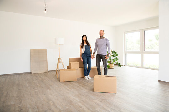 Couple with cardboard boxes and electric lamp standing in new home