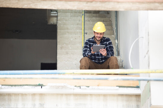 Construction worker using digital tablet while sitting on steps at construction site