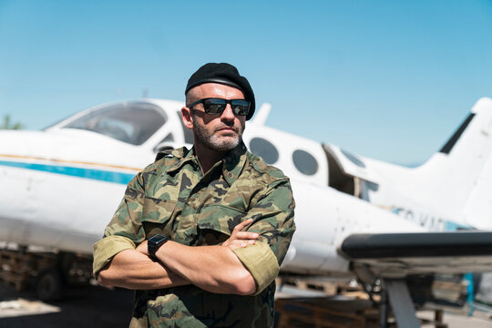 Confident army soldier standing with arms crossed against airplane on sunny day