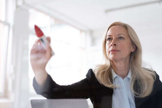 Female entrepreneur writing on window with felt tip pen in home office seen through glass