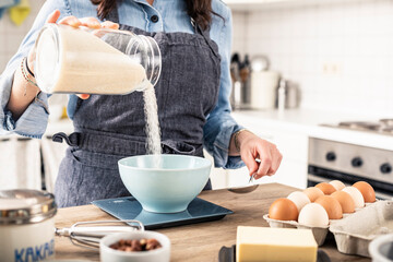 Woman weighing flour on kitchen scale for making cake at home