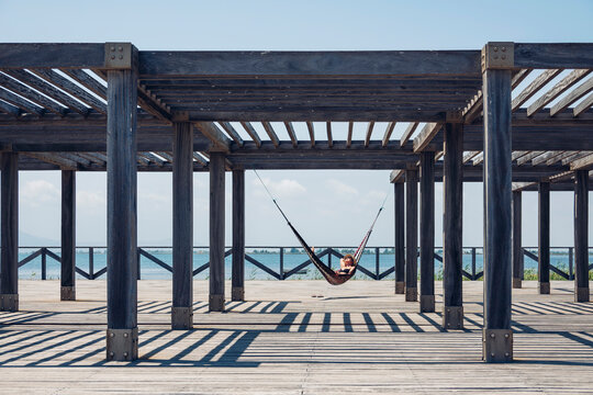 Woman lying in hammock hanging from metallic structure on boardwalk during sunny day
