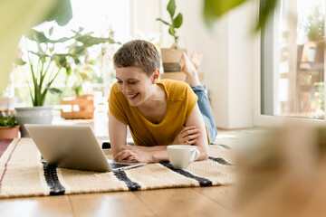 Smiling mid adult woman using laptop while lying on carpet at home