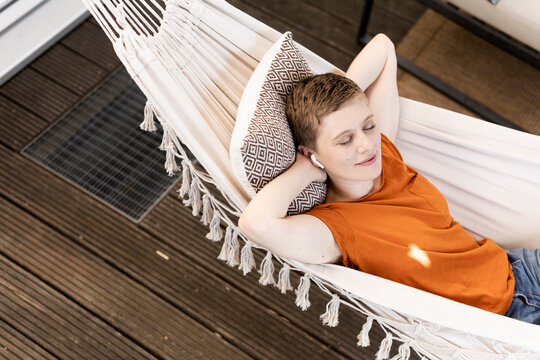 Woman with eyes closed listening music through wireless headphones while lying on hammock in porch