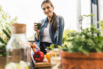 Smiling young woman holding juice while sitting against clear sky in yard