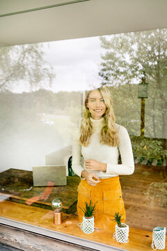 Smiling female entrepreneur standing in office seen through window
