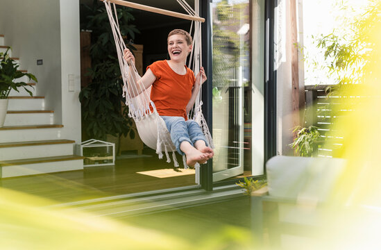 Cheerful woman with short hair laughing while swinging against house in porch