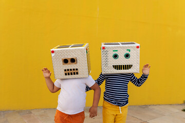 Friends wearing robot costumes waving while standing against yellow wall