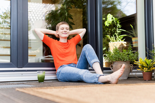 Woman with eyes closed relaxing while sitting against house door in porch