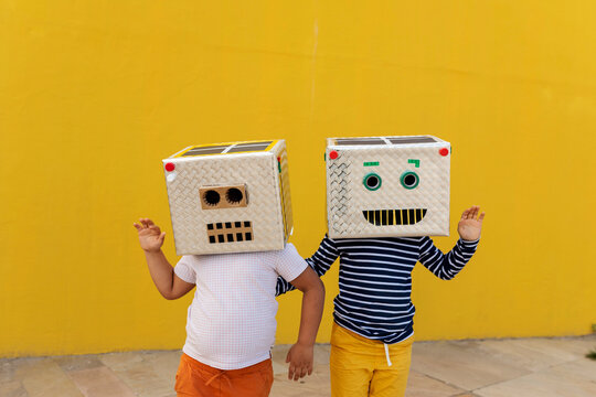 Friends Wearing Robot Costumes Waving While Standing Against Yellow Wall