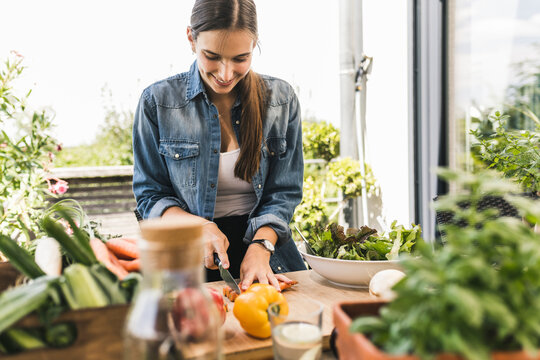Smiling young woman chopping vegetables on cutting board in yard