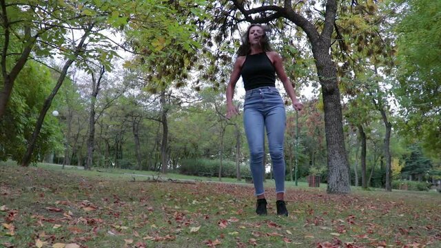 Female dancer dances with jumping and kicking her legs in the air in a park. Hip dance moves.