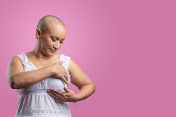 Mujer con cáncer de mama en fondo rosado realizando autoexamen de mama - obrazy, fototapety, plakaty