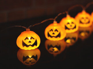 Halloween pumpkin string lights glowing with reflection on the table. selective focus. Halloween decoration concept.