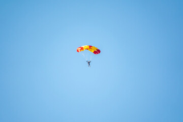 Fototapeta na wymiar One parachutist floats slowly at low altitude on the background of clear sky