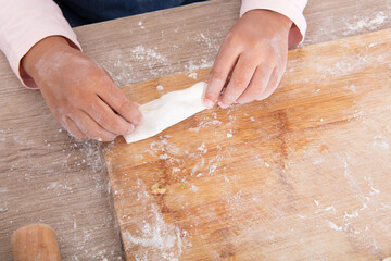 Looking down on a pair of small hands making dumplings on a cutting board