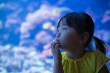 水族館の水槽で泳ぐ魚を見つめる子ども