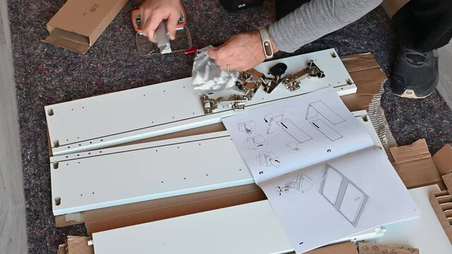Turin, Italy. October 2020. Scenes at home: assembly of a piece of furniture, the Caucasian man takes the small parts out of the box and checks the quantity. Next to the assembly manual.