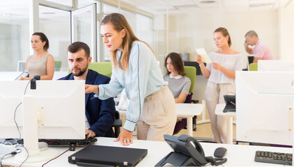 Happy girl helping male colleague in work with computer in modern coworking space