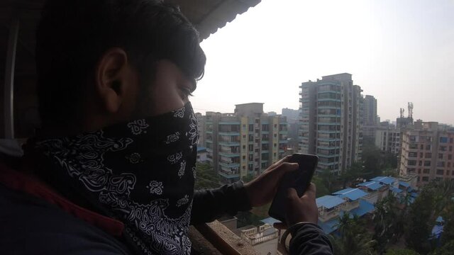 boy using mobile on terrace waring mask India looking over buildings new normal