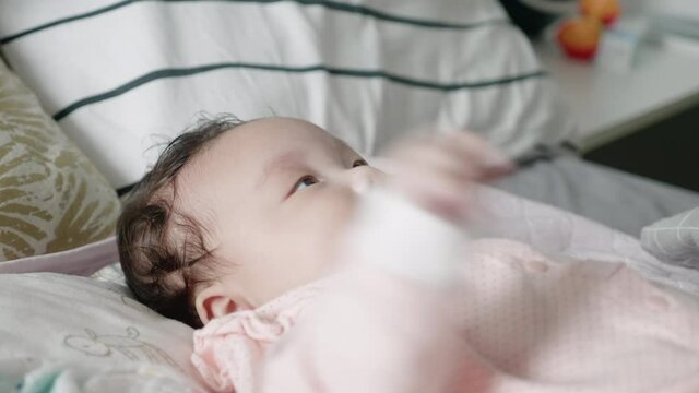 Medium shot, side angle of a 2 month old mixed Korean baby lying in bed happily watching an electronic mobile rotate.