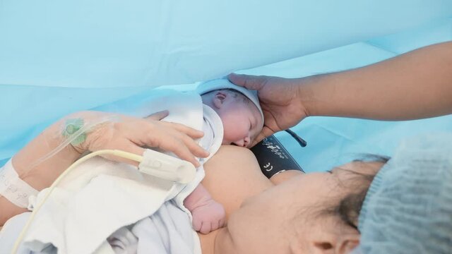 Medium-Wide shot of a newborn baby feeding for the first time after birth with the support of the husband.