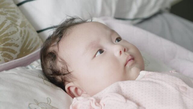 Medium-close reverse shot of a 2 month old mixed Korean  baby lying in bed happily watching an electronic mobile rotate.