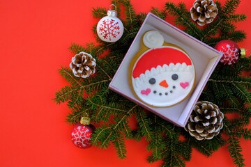 Christmas and New Years concept. Christmas gingerbread and cookies. Sweets for the winter holidays. snowman gingerbread in a box, cones, red festive balls and fir branches on a  red background