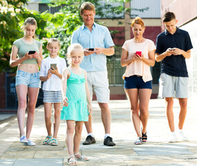 Happy parents with four kids in different age looking at mobile phones outdoors in town. Focus on little girl