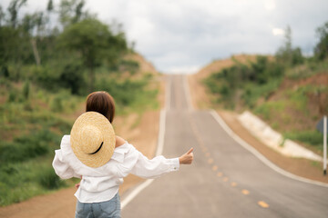 Fototapeta premium Woman hitchhiking on the road, empty rural curve, asphalt road way. Rear view.