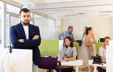 Portrait of confident businessman with arms crossed in busy modern coworking space