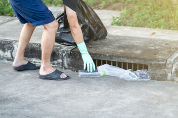 Man hand keeping plastic waste in a sewer drain into black bag.