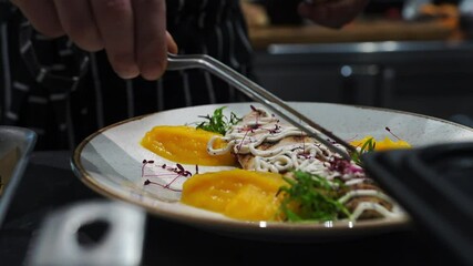 Cook inside kitchen working area, hands decorating fried cod fillet yellow pumpkin puree with purple microgreens before serving waiter client. Working environment, weekend, full boarding many orders