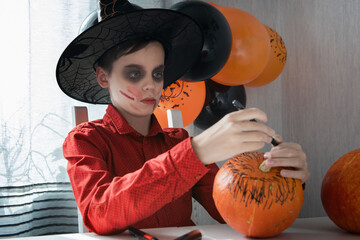 Happy teen boy in costume preparing for the Halloween celebration drawing a pumpkin. Halloween...