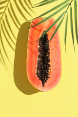 Papaya tropical fruit with deep shadows from palm leaf on pastel yellow background .