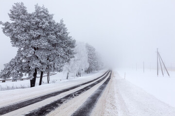 Snow-covered asphalt road through the country fields in a fog after a blizzard.