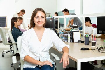 Young happy smiling woman sitting at her workplace in office