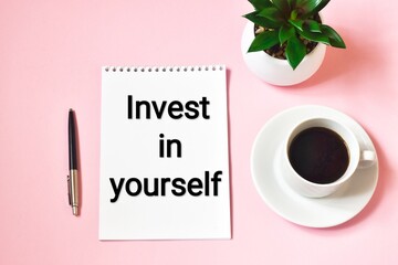 Invest in yourself - advice or reminder - writing on a notepad with cup of coffee against pink background. Concept business, investment.