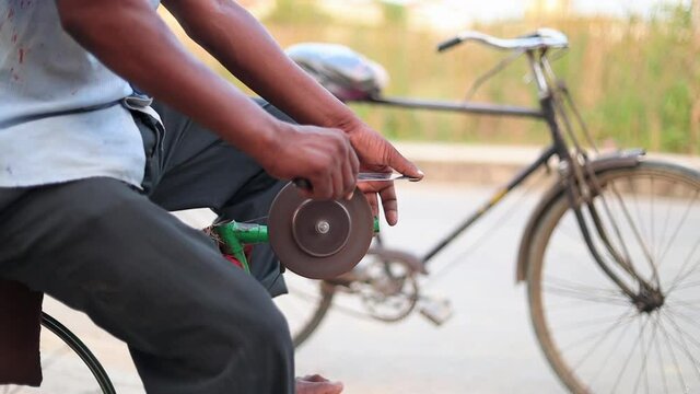 Closeup hands of a man sharpening a knife on a DIY makeshift sharpening machine on a bicycle frame.