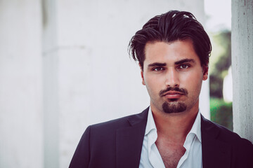 Portrait of young man with trendy style. Trendy hair and goatee. He wears a white shirt and jacket.