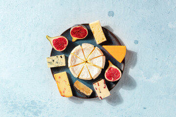 Cheese plate, shot from the top with a place for text. A selection of soft and hard cheeses with figs on a light blue background