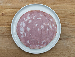 Slices of sausage italian Mortadella in a white dish on wooden table. Top view
