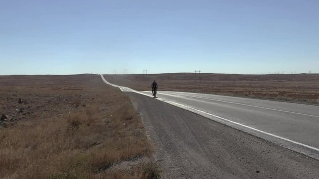 A lone man cycling slowly cross the Kazakh steppe as the road stretches on for as far as the eye can see