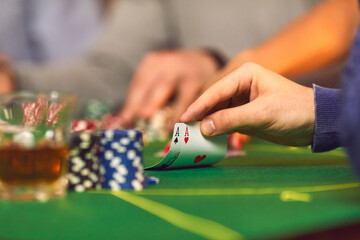 Closeup of gambler's hand holding a pair of aces while playing poker on casino night