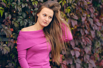 young beautiful woman in a pink knitted sweater looks to the side, against the background of wild...